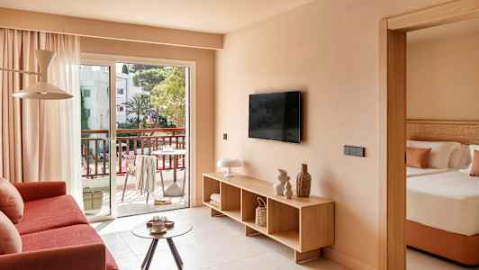 Vardagsrum med soffa, TV och utgång till balkong, samt ett delvis synligt sovrum. (AI-genererad text)