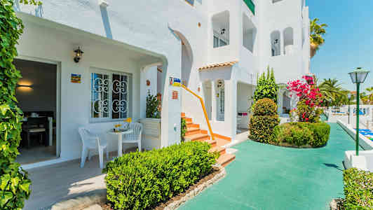 Vit byggnad med terrasser och en grönskande omgivning. (AI-genererad text)