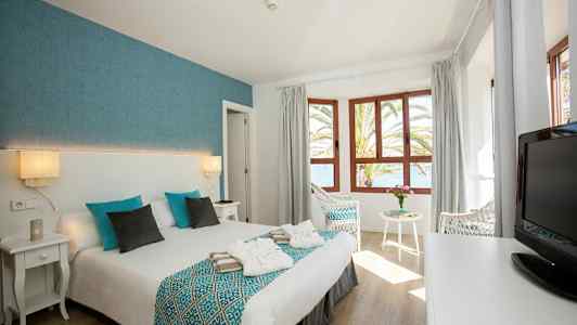 Hotellrum med dubbelsäng, fönster och utsikt över havet. (AI-genererad text)