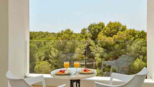 Två stolar och ett bord med frukost serverad med utsikt över en skog. (AI-genererad text)