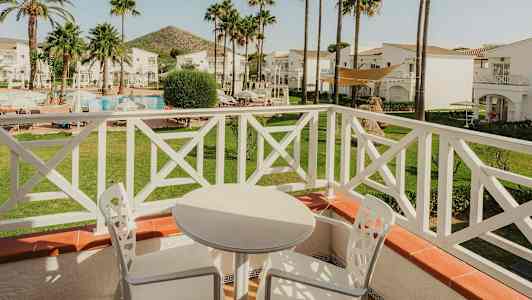 Utsikt från en balkong med vita utemöbler, mot en trädgård med pool och palmer. (AI-genererad text)