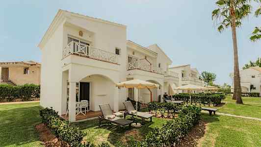 Hotellets vita, tvåvåningsbyggnader med balkonger och uteplatser omgivet av grönska. (AI-genererad text)