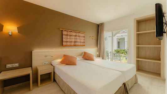 Ett hotellrum med två enkelsängar, dekorativa kuddar och en vägg med konst. Fönster med utsikt över en trädgård. (AI-genererad text)