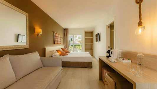 Ett hotellrum med en soffa, en säng, ett skrivbord med kaffemaskin och glas, samt en dörr till en balkong. (AI-genererad text)