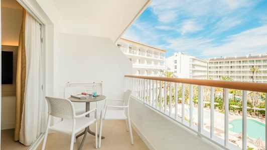 En möblerad balkong med två stolar och ett bord, med utsikt över hotellområde och pool. (AI-genererad text)