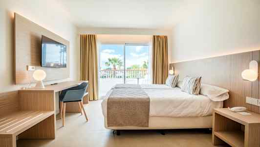 Modernt inrett hotellrum med säng, skrivbord och stora glasdörrar mot en balkong. (AI-genererad text)