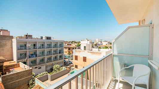 Utsikt från en balkong som visar ett bostadsområde med byggnader och träd under en klar blå himmel. (AI-genererad text)