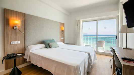 Hotellrum med två sängar, havsutsikt genom en glasdörr och skrivbord. (AI-genererad text)