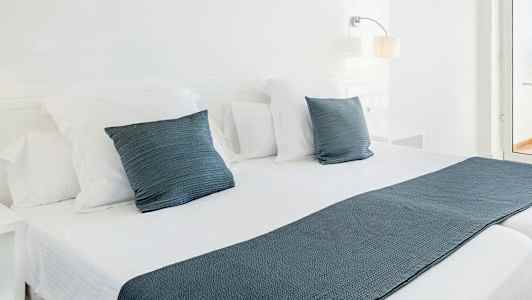 Vita sängkläder på en dubbelsäng med blå prydnadskuddar och överkast. (AI-genererad text)