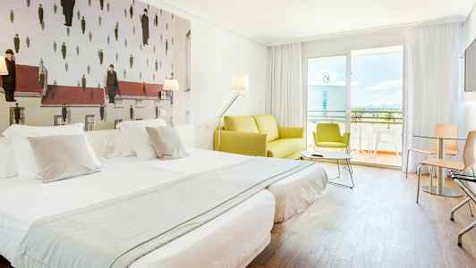 Ett hotellrum med två bäddade enkelsängar, en grön soffa och en balkong i bakgrunden. Väggdekorationen har ett konstverk med en ovanlig design. (AI-genererad text)