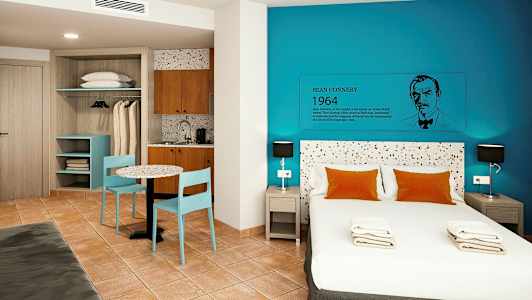 Ett modernt hotellrum med en dubbelsäng, blå väggar och en liten kökshörna. (AI-genererad text)