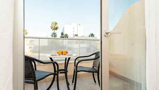 En balkong med två stolar och ett bord, där drycker serveras. (AI-genererad text)