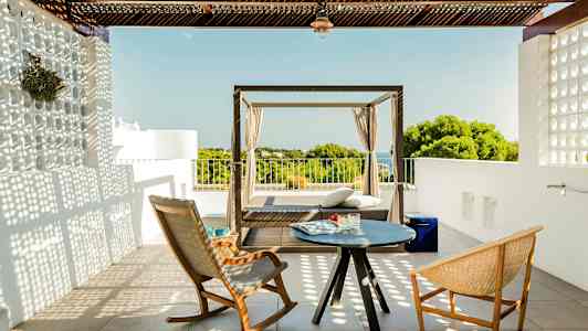 En terrass med två stolar och ett litet bord samt en dagbädd med utsikt över grönska och hav. (AI-genererad text)