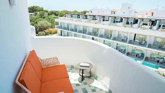 Bilden visar en balkong med orange sittmöbler och ett runt bord, med utsikt över en vit byggnad med flera våningar och balkonger. (AI-genererad text)