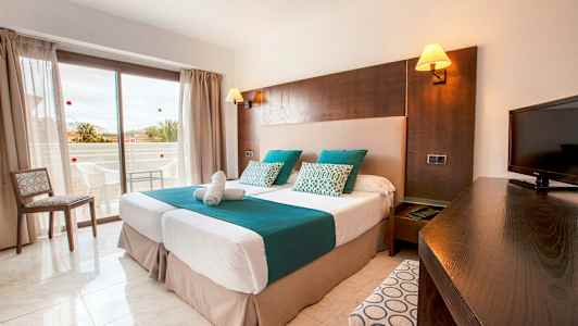 Ett hotellrum med två enkelsängar, en TV och en balkong i bakgrunden. (AI-genererad text)