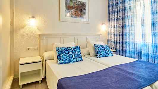 Bild av sovrum med två enkelsängar, blå kudde och täcke, samt blå gardiner. (AI-genererad text)