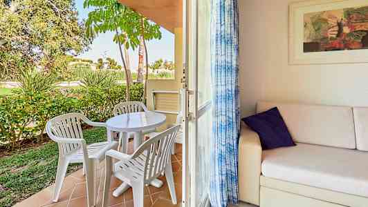 En terrass med plastmöbler och en trädgård samt en inomhusdel med soffa och konst på väggen. (AI-genererad text)