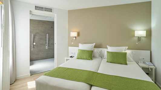 Hotellrum med två enkelsängar, gröna sängkläder och en öppning mot badrummet. (AI-genererad text)