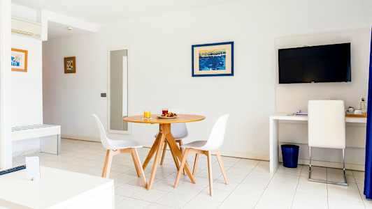 Ett ljust rum med ett runt matbord och stolar, en TV på väggen och en arbetsyta med en stol. (AI-genererad text)