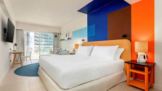 Ett hotellrum med en dubbelsäng, färgglad väggdesign och en balkong. (AI-genererad text)