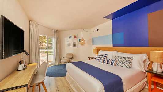 Bild av ett hotellrum med modern inredning, en säng med blå överkast, skrivbord och stol samt en balkongdörr. (AI-genererad text)