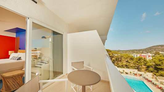 Utsikt från en balkong med bord och stolar, med en pool och byggnader i bakgrunden. (AI-genererad text)