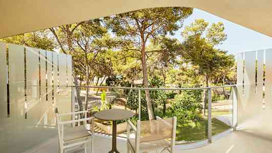 En balkong med två stolar och ett bord, med utsikt över en grönskande trädgård. (AI-genererad text)