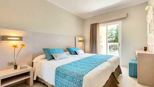 Ett hotellrum med en dubbelsäng, blå dekorativa kuddar och ett blått överkast. (AI-genererad text)