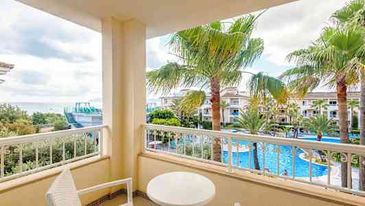 Balkong med utsikt över poolområde och palmer. (AI-genererad text)