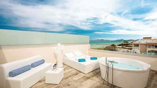 Takterrass med utsikt över havet, utrustad med jacuzzibad, solstolar och soffområde. (AI-genererad text)