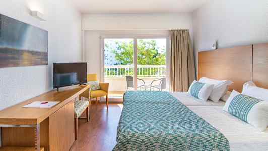 Hotellrum med två bäddar, skrivbord, och fönster med utsikt mot balkong. (AI-genererad text)