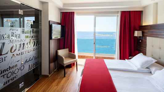 Ett hotellrum med stora sängar, röd inredning och en balkong med utsikt över havet. (AI-genererad text)