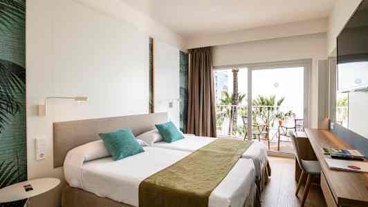 Hotellrum med två enkelsängar, skrivbord och balkong med utsikt mot palmer. (AI-genererad text)