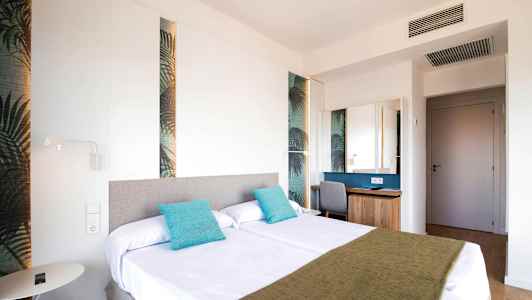 Ett hotellrum med två sängar dekorerade med turkosa kuddar och en grön sängfilt. (AI-genererad text)