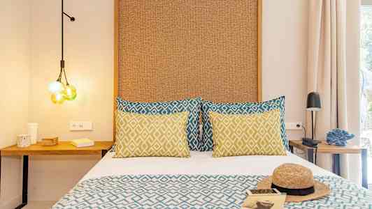 Ett rum med en säng klädd med mönstrade kuddar och täcke, samt nattduksbord och dekorativa detaljer. (AI-genererad text)