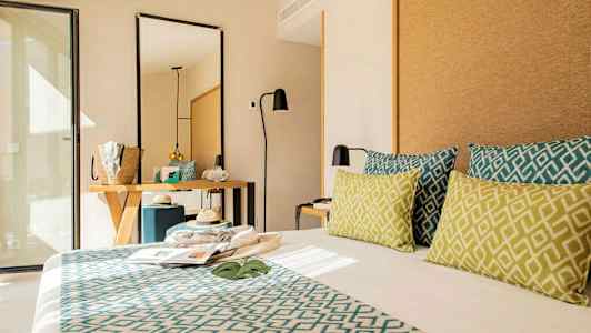 Hotellrum med modern inredning, säng med dekorativa kuddar, spegel och skrivbord. (AI-genererad text)