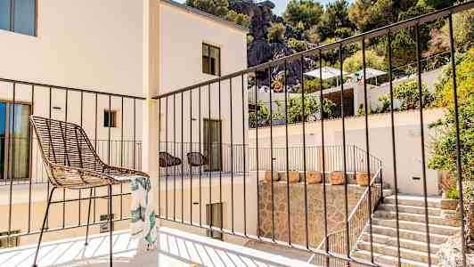 En balkong med en stol och ett räcke, omgiven av en byggnad och grönska. (AI-genererad text)