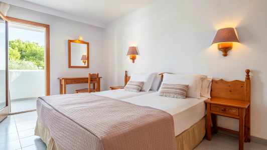 Ett hotellrum med en dubbelsäng, två sänglampor, ett skrivbord, en stol och en balkong. (AI-genererad text)