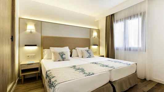 Modernt inrett hotellrum med en dubbelsäng, sängbord och ett fönster med ljusa gardiner. (AI-genererad text)