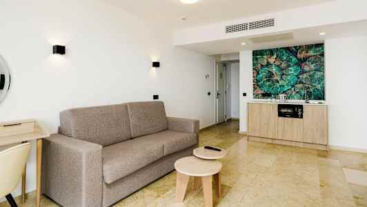 Ljus lägenhet med grå soffa, skrivbord och köksdel. (AI-genererad text)