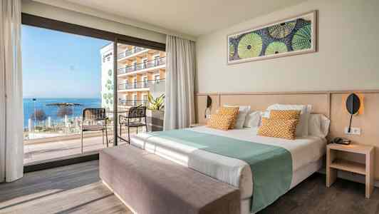 Hotellrum med säng, sittmöbler och en utsikt mot havet genom stora fönster. (AI-genererad text)