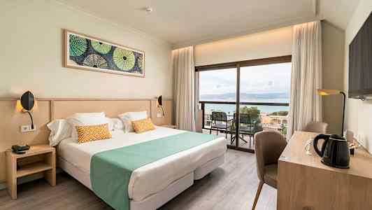 Bild av ett hotellrum med dubbelsäng, skrivbord och utsikt mot havet. (AI-genererad text)