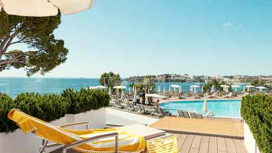 En solstol med gulvit handduk och strandväska står på en terrass med utsikt över en pool och havet. (AI-genererad text)