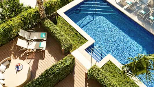 Ett poolområde med solstolar och gröna buskar. (AI-genererad text)