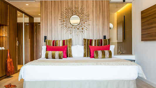 Modernt hotellrum med en stor säng, dekorativa kuddar i olika färger och träpanel på väggen bakom. (AI-genererad text)