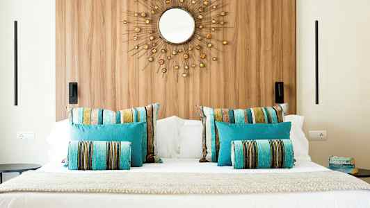 Bild av en säng med färgglada kuddar och en dekorativ spegel på väggen. (AI-genererad text)