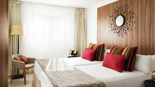 Modern hotellrum med två sängar, färgstarka kuddar och minimalistisk inredning. (AI-genererad text)