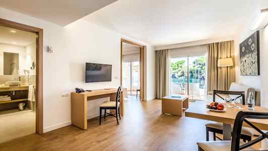 En modern hotellsvit med sittgrupp, matbord, TV och öppning mot balkong med utsikt. (AI-genererad text)