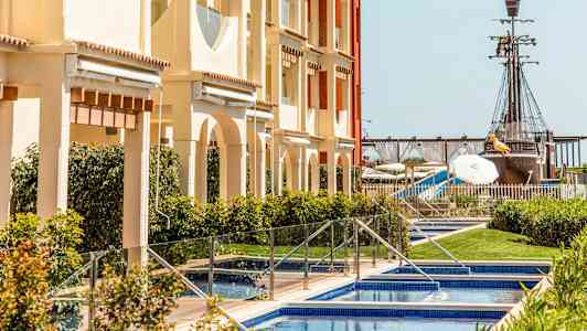 En byggnad med pooler framför, och i bakgrunden syns ett piratskepp. (AI-genererad text)