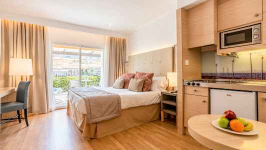 Ett hotellrum med en stor säng, skrivbord, och ett kök, samt en balkong med utsikt. (AI-genererad text)